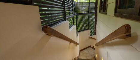 A staircase with wooden handrails and a tiled floor, leading to a room with a window and blinds.