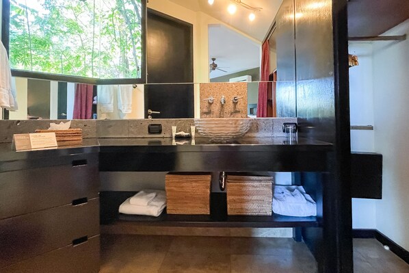 A modern bathroom with a large mirror, a sink with a stone basin, and a vanity with drawers and baskets. - Tulemar Resort (Quepos)