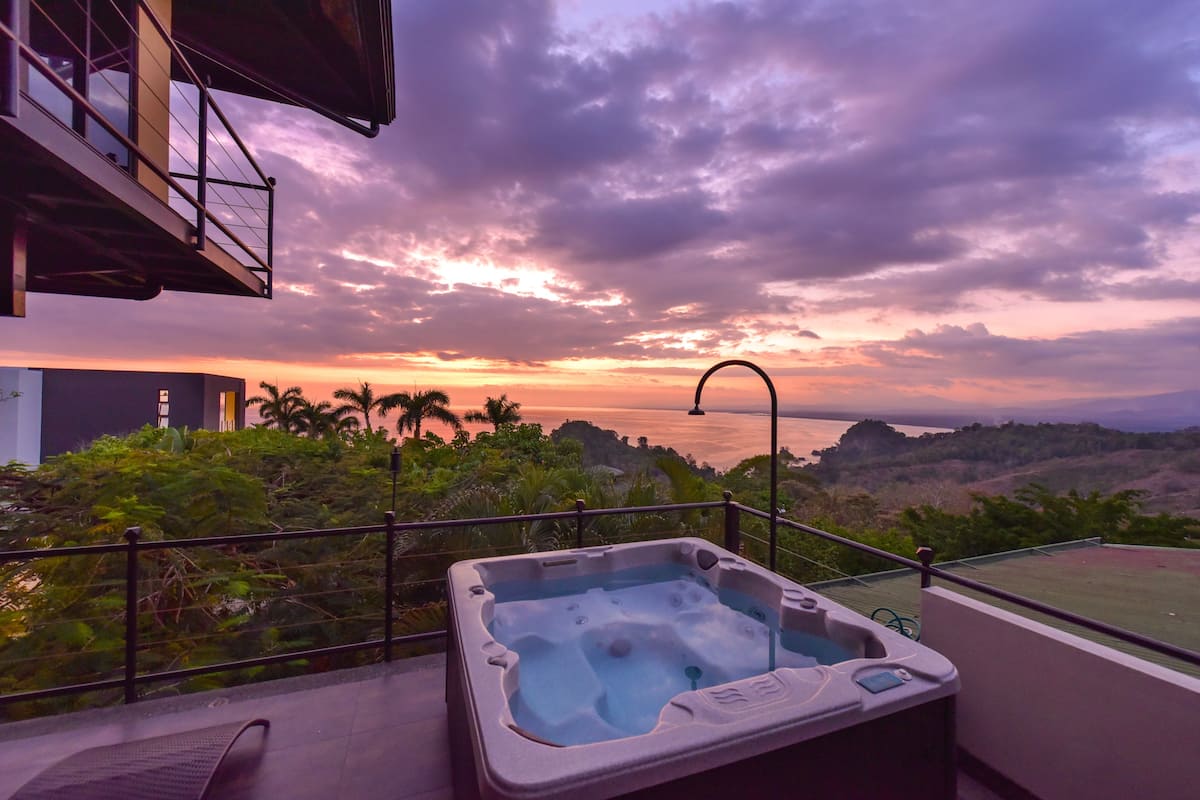 Un jacuzzi en un balcón con vista al atardecer sobre el océano.