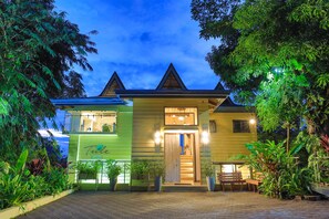 A two-story house with a green facade, a wooden front door, and a staircase leading to the upper floor.