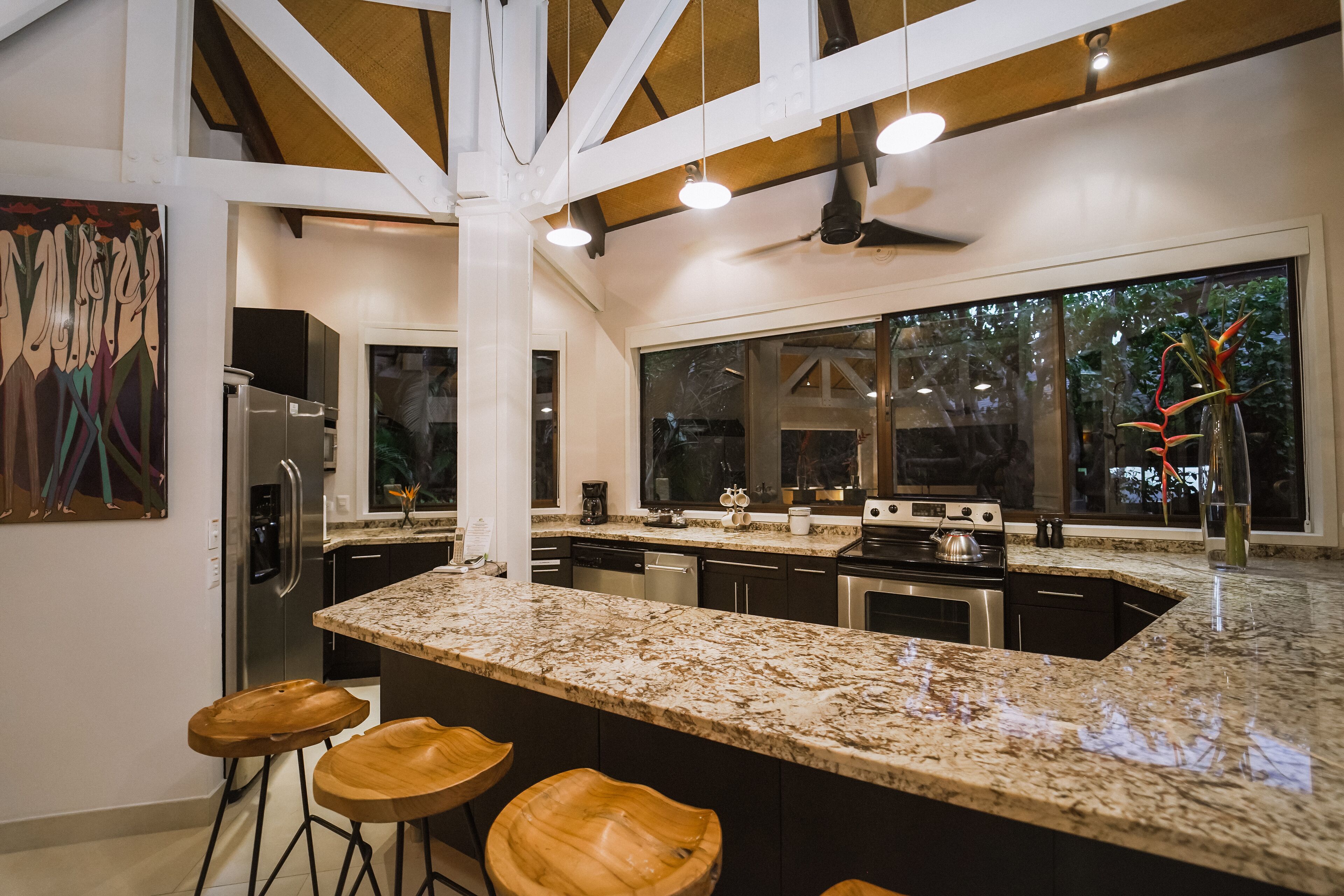 Una cocina moderna con una isla grande, taburetes de bar y vistas al exterior a través de amplios ventanales.