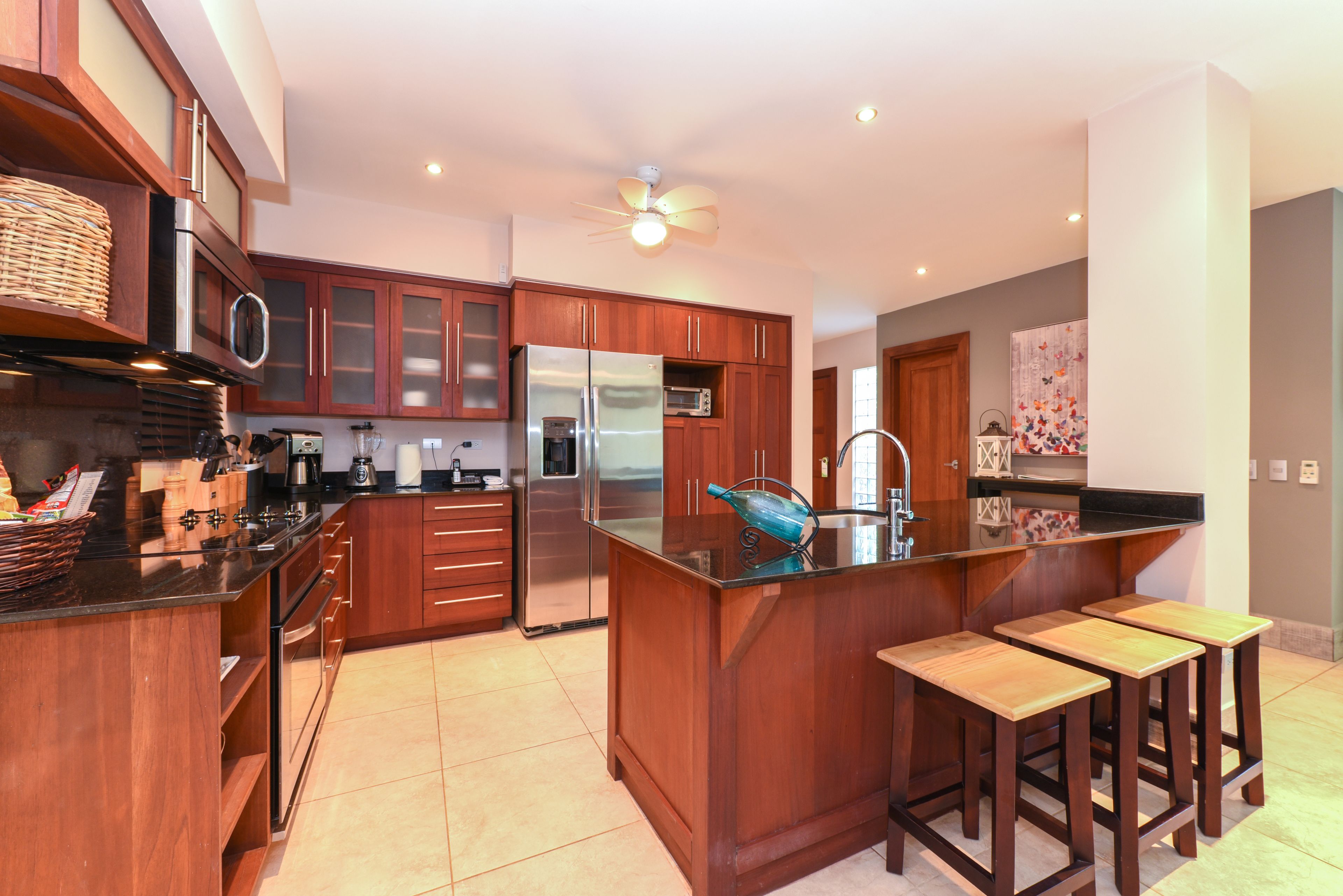 Una cocina moderna con armarios de madera, un refrigerador de acero inoxidable, un microondas y una isla grande con taburetes.
