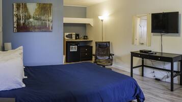 A bedroom with a bed, a desk, a chair, a television, and a microwave.