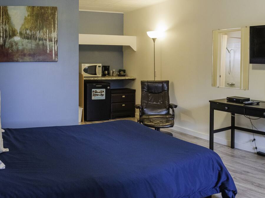 A bedroom with a bed, a desk, a chair, a television, and a microwave.
