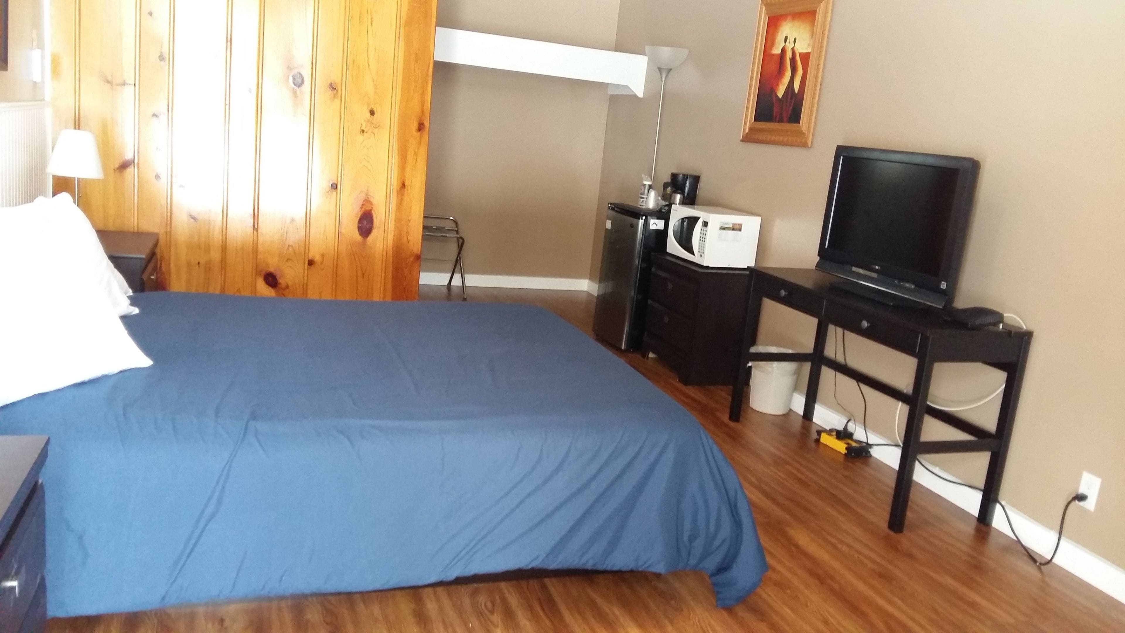 A bedroom with a bed, a desk, a television, and a microwave.