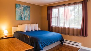 Habitación de hotel con cama, una mesa, una lámpara, un cuadro y una ventana con cortinas.