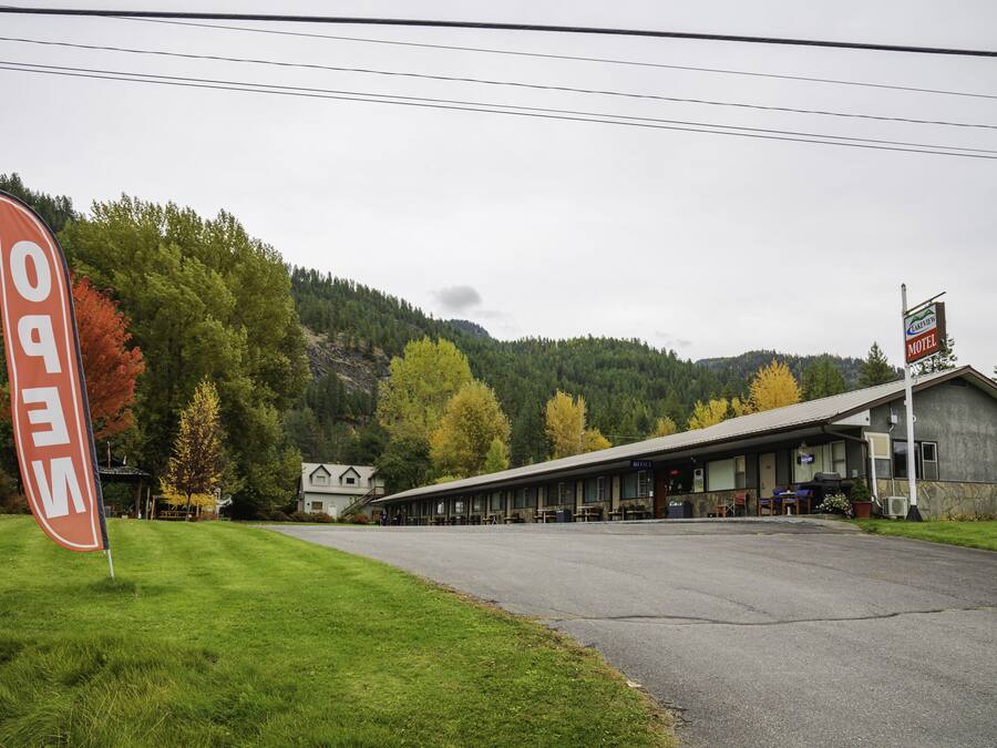 Et motel med en lang, etetages bygning, et overdækket udendørs siddeområde og et bjerglandskab i baggrunden.