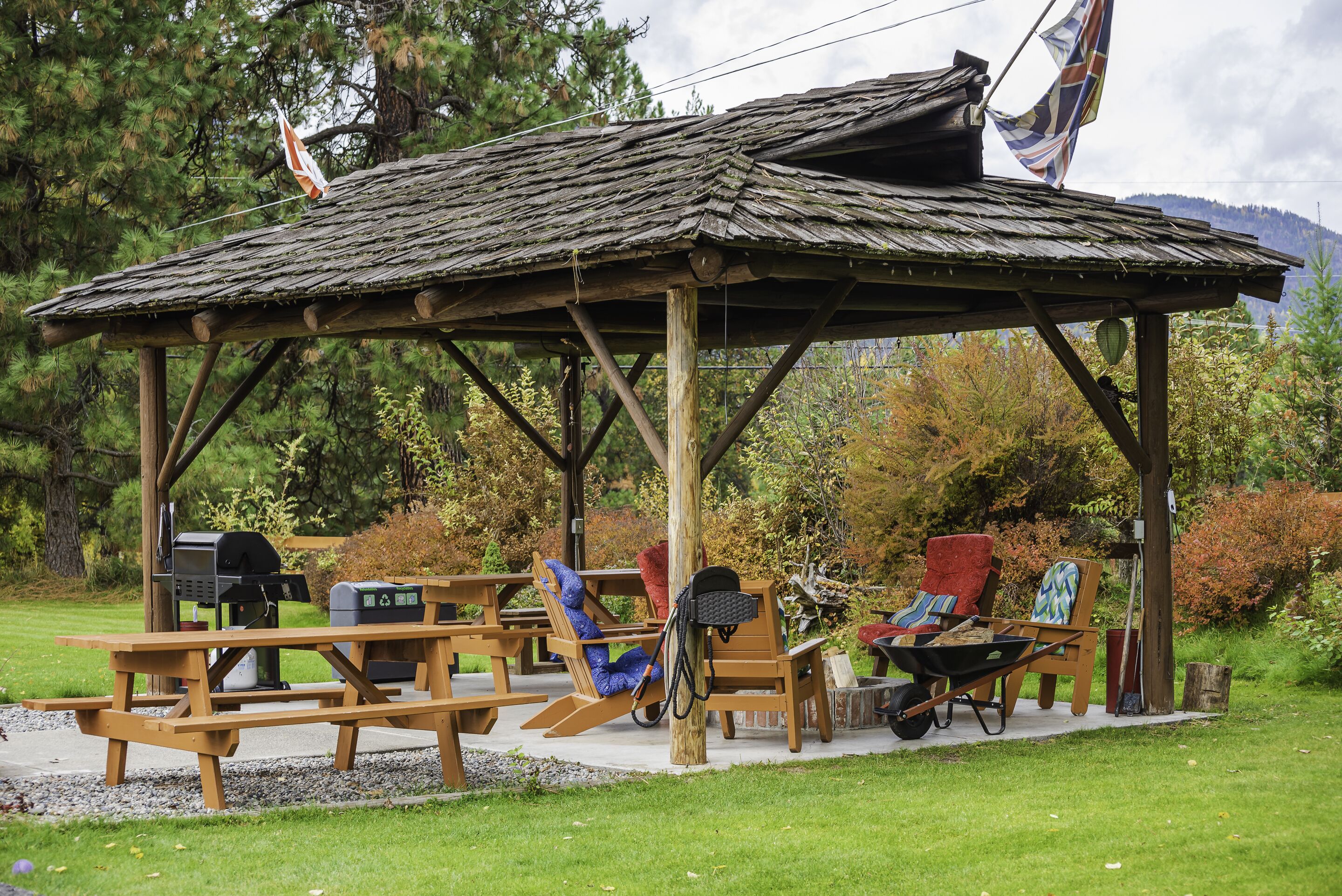 Un padiglione di legno rustico con tavoli e sedie da picnic, un barbecue e una carriola.