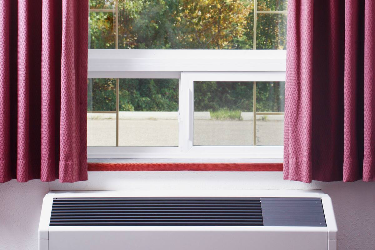 A room with a window, a white air conditioner, and red curtains.