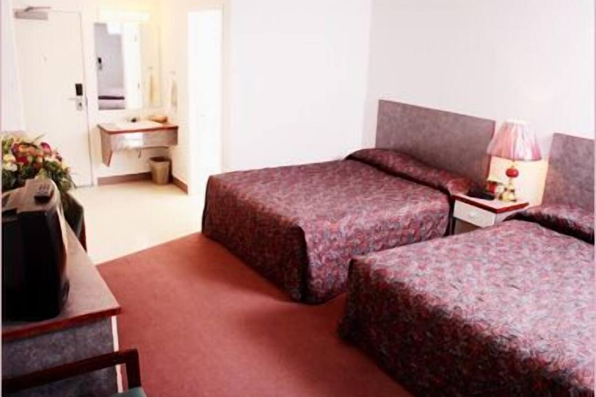 A hotel room with two beds, a desk, a chair, a lamp, and a mirror.