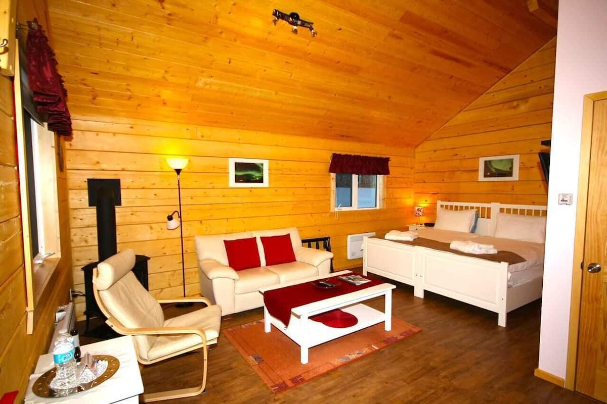 A cozy log cabin interior with a sofa, armchair, and a bed.