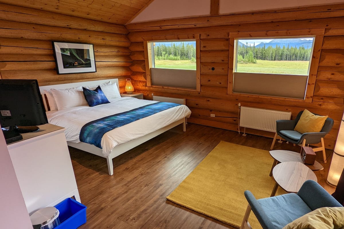 A cozy log cabin bedroom with a bed, a chair, a small table, and a TV.