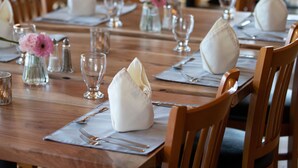 Un espace repas avec des tables en bois disposées pour accueillir plusieurs convives, agrémenté de serviettes blanches, de verres transparents et de petits vases avec des fleurs.