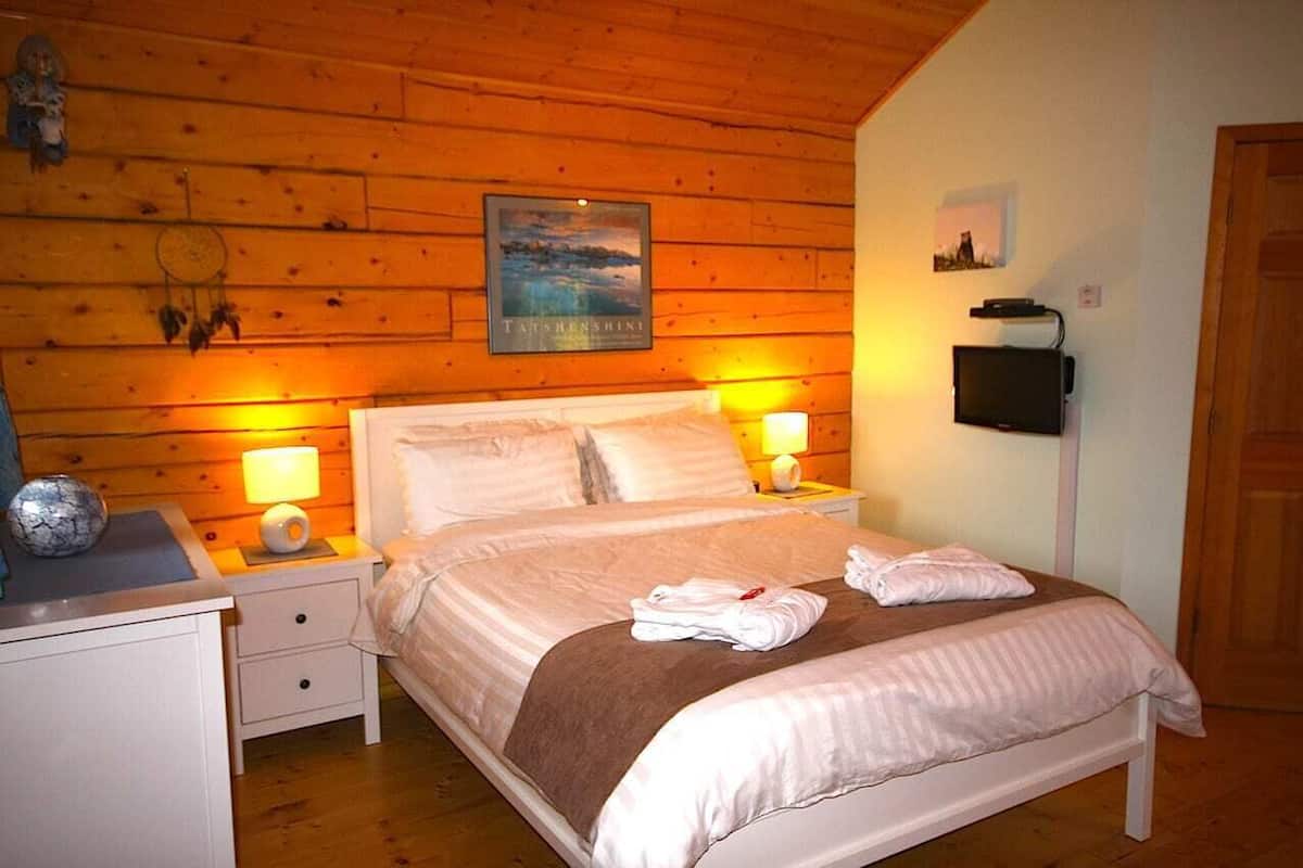 A cozy bedroom with a wooden ceiling, a bed with white linens, two bedside lamps, and a framed picture on the wall.
