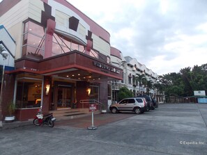 Un hotel con fachada roja y blanca, un letrero de 'No Estacionar' y un coche estacionado.