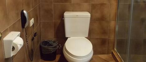 Ein Badezimmer mit Toilette, Handtrockner, Mülleimer und einer Duschkabine aus Glas.