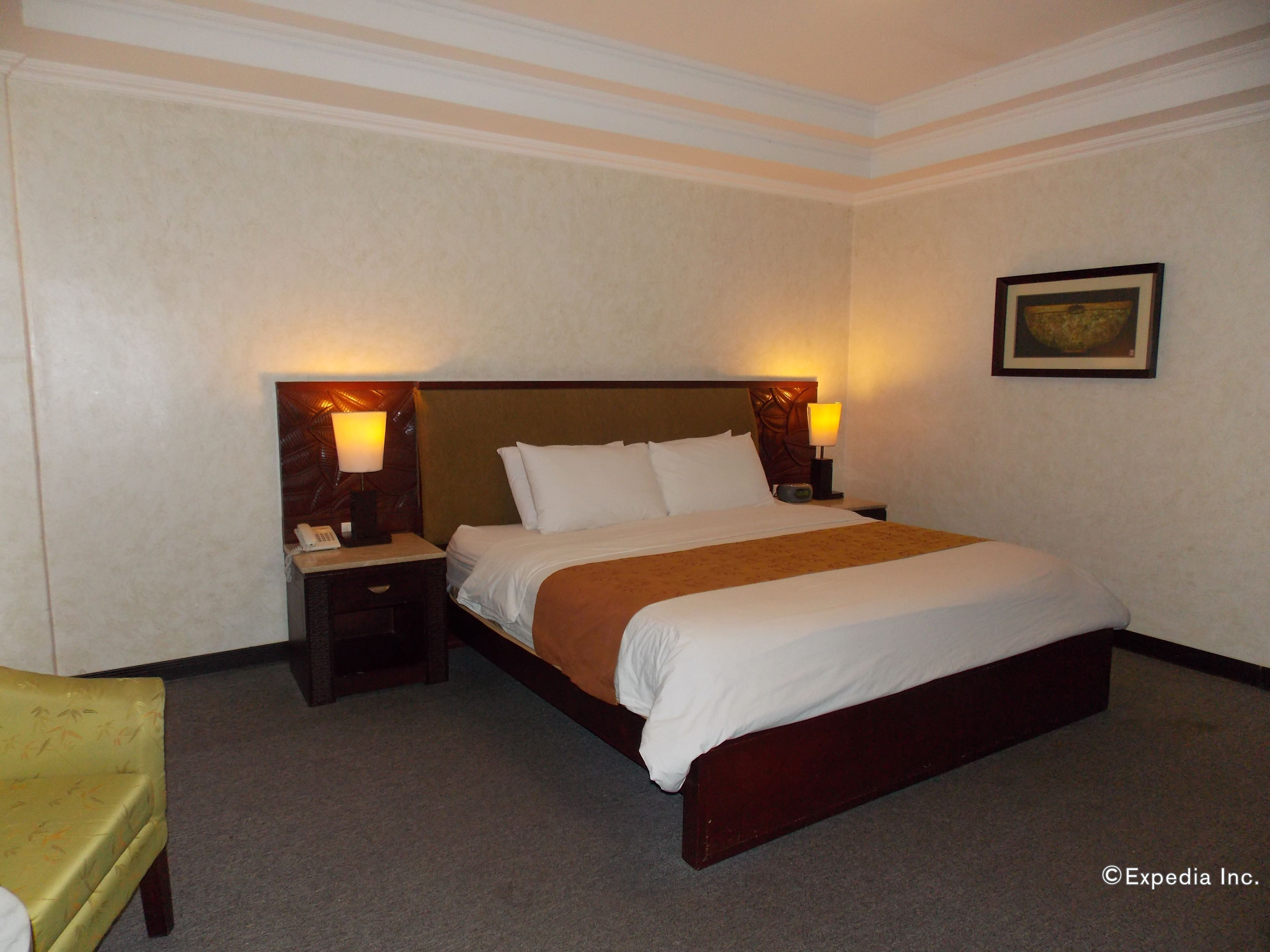 Habitación de hotel con una cama grande, dos mesitas de noche con lámparas, una silla y un cuadro enmarcado en la pared.