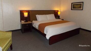 Habitación de hotel con una cama grande, dos mesitas de noche con lámparas, una silla y un cuadro enmarcado en la pared.