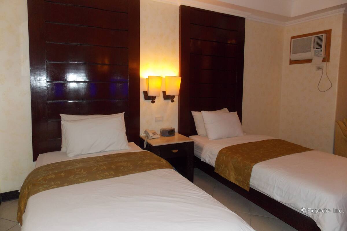Habitación de hotel con dos camas, una mesita de noche, un teléfono y lámparas fijadas a la pared.