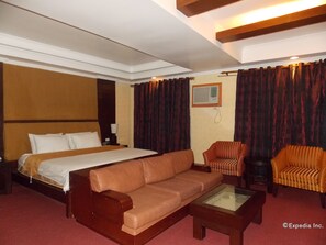 Habitación de hotel con una cama grande, un sofá, dos sillones, una mesa de centro y un equipo de aire acondicionado en la pared.