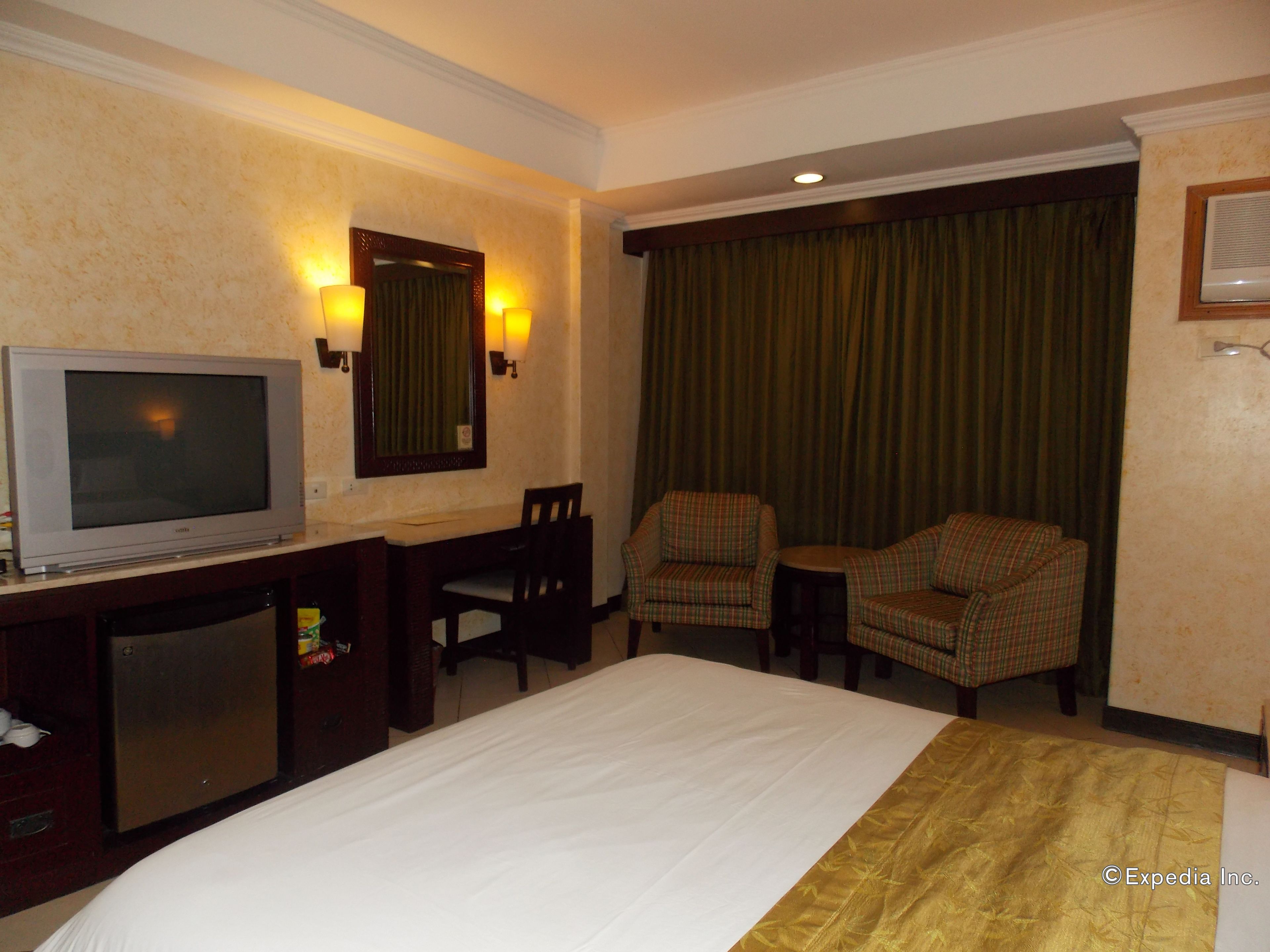 A hotel room with a bed, a television, two armchairs, a desk, and a small table.