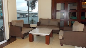 A lobby with a seating area featuring sofas and a coffee table, large windows with a view of the street, and a wooden door with a mirror. - MO2 Westown Hotel Bacolod - Mandalagan (Bacolod)