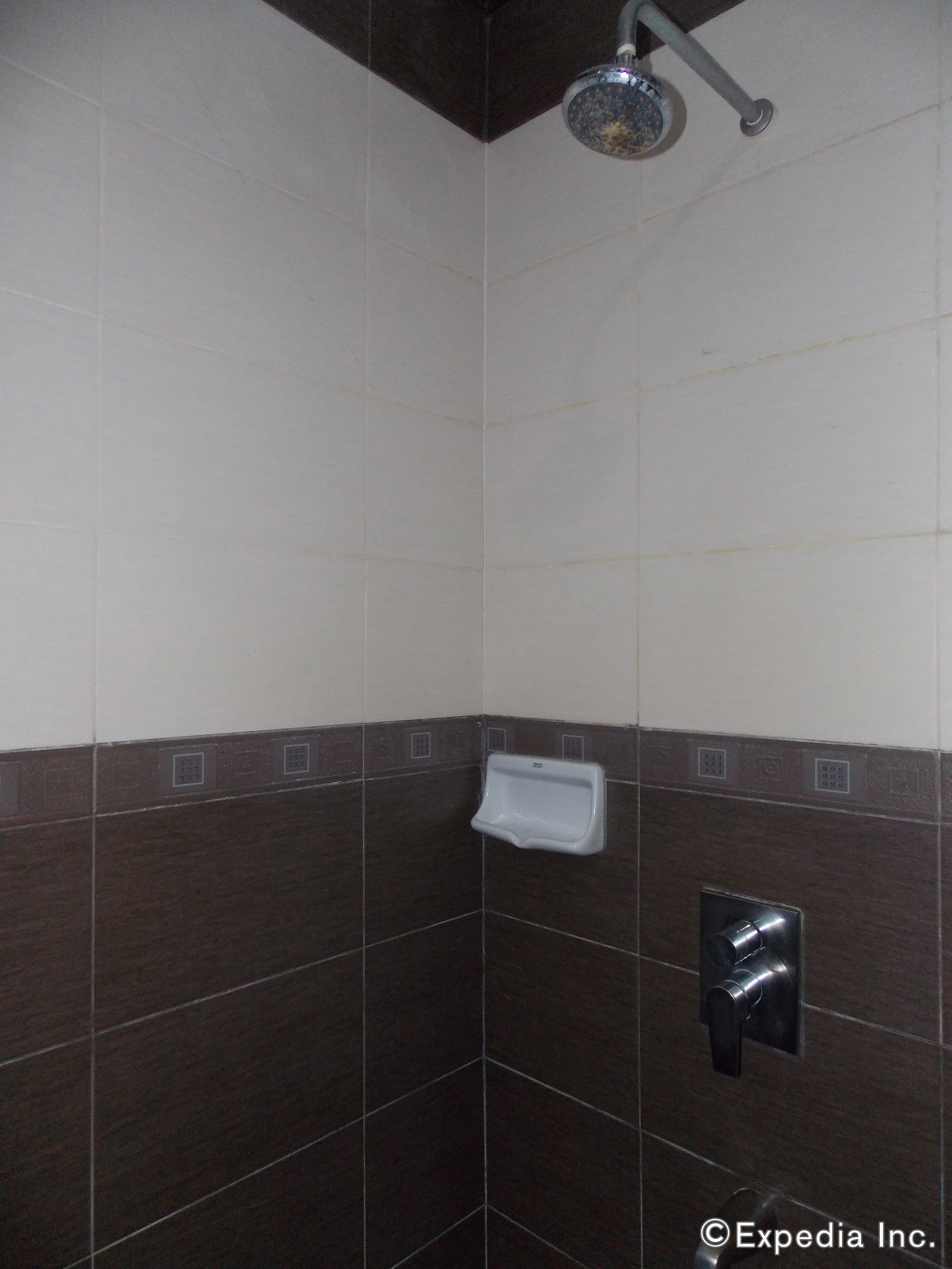A shower with a handheld showerhead, a paper towel dispenser, and a towel rack.
