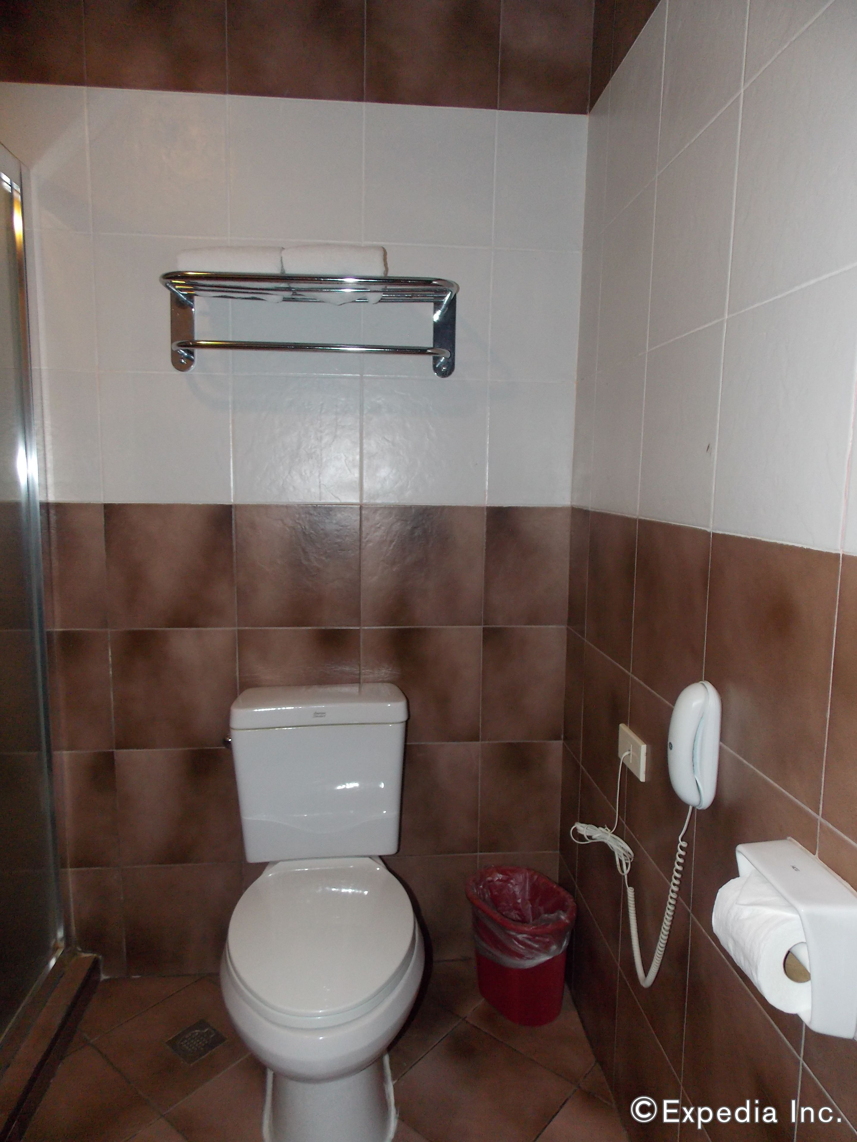 Un baño con inodoro, un cubo de basura, secador de manos y dispensador de toallas de papel.