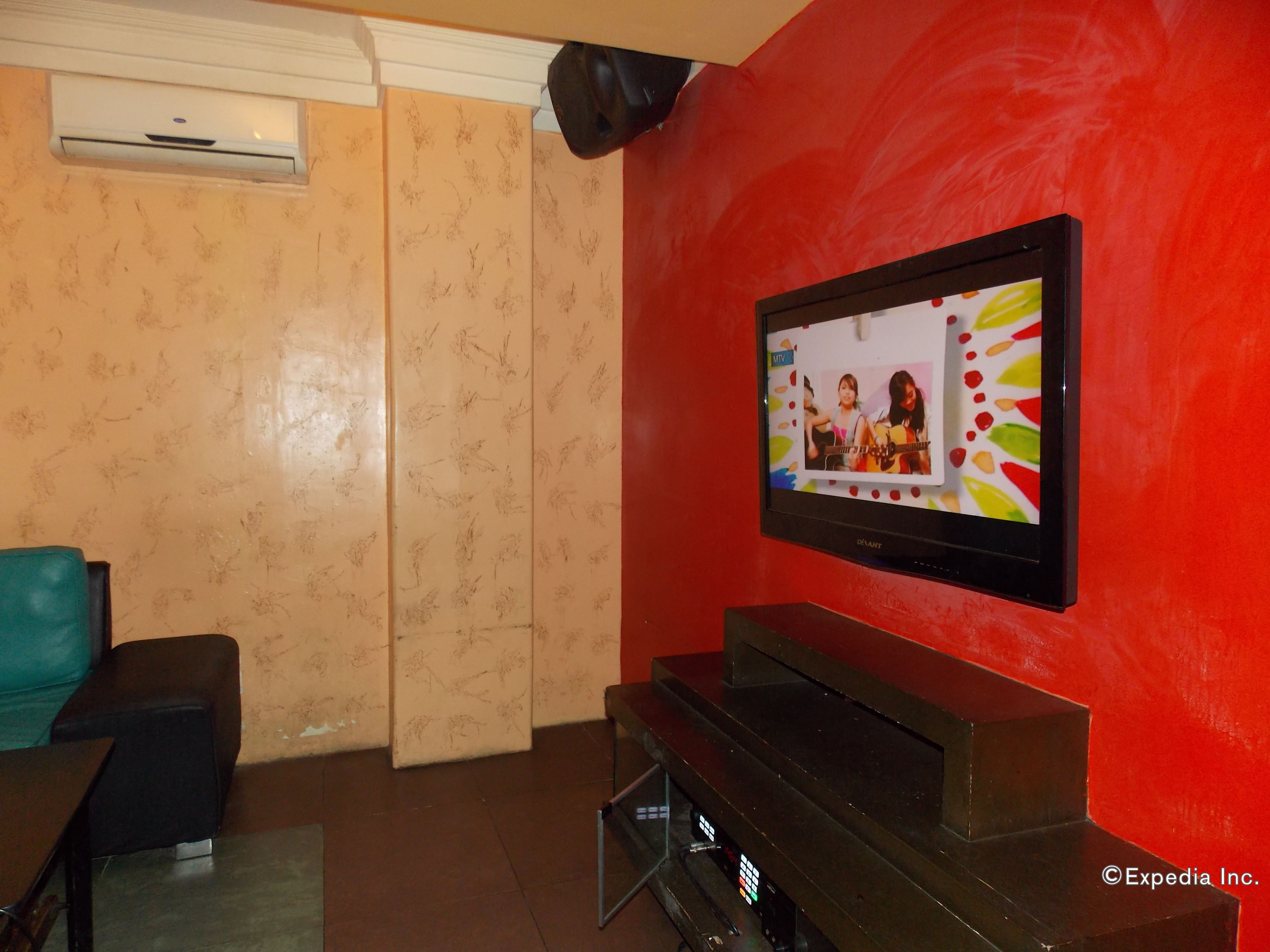 Un salón con un televisor de pantalla plana montado en una pared roja, un mueble de entretenimiento negro y una pared beige con estampado.