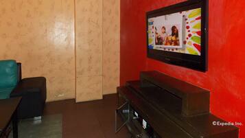 Un salón con un televisor de pantalla plana montado en una pared roja, un mueble de entretenimiento negro y una pared beige con estampado.