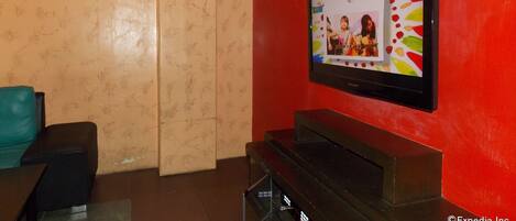 A living room with a flat-screen TV mounted on a red wall, a black entertainment unit, and a beige patterned wall.