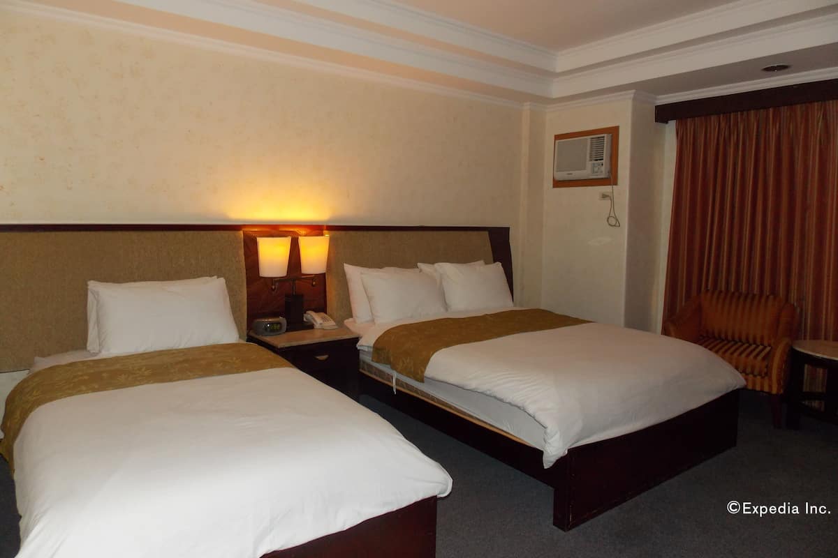 Habitación de hotel con dos camas, una mesita de noche con lámpara, teléfono y aire acondicionado.