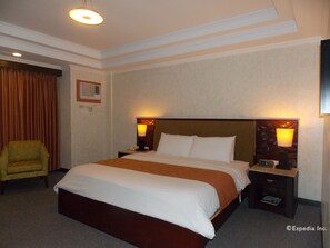 Habitación de hotel con una cama grande, dos mesitas de noche, una silla y un televisor en la pared.