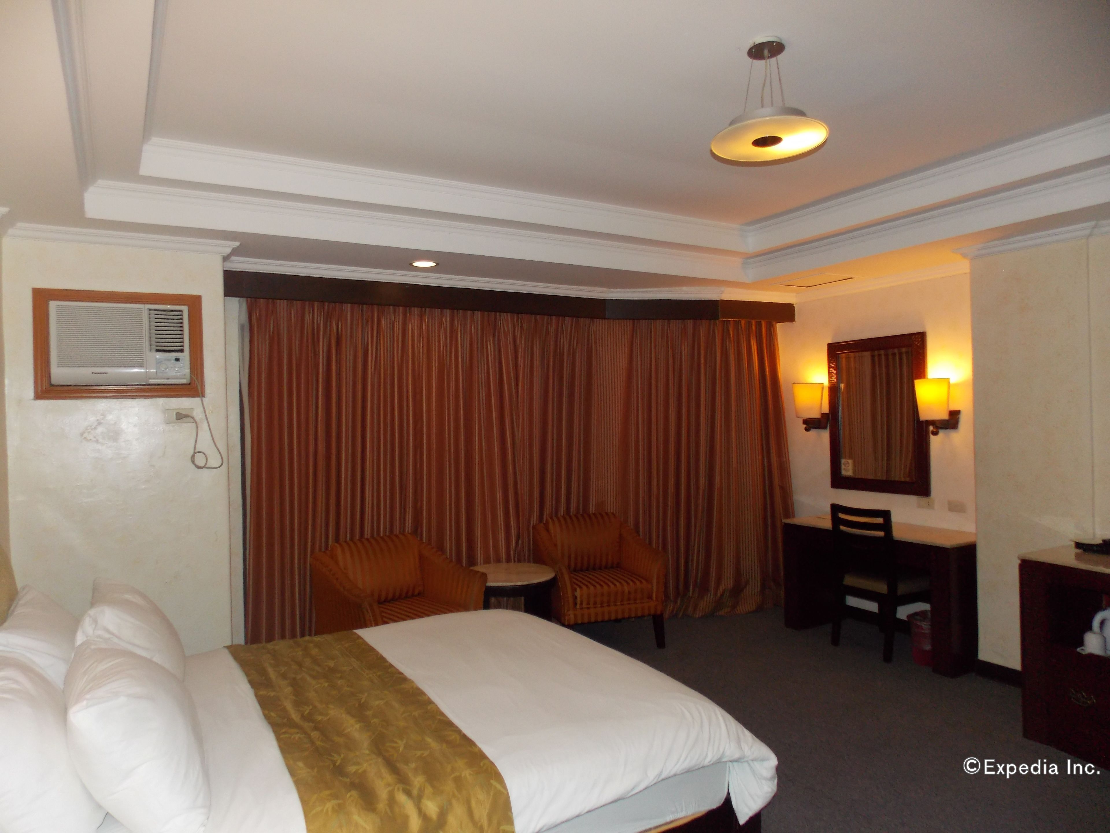 A hotel room with a bed, two armchairs, a small table, a desk, and a mirror.