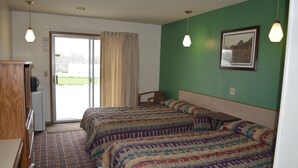 Habitación de hotel con dos camas, un escritorio, una silla y vistas al exterior a través de una puerta corrediza.