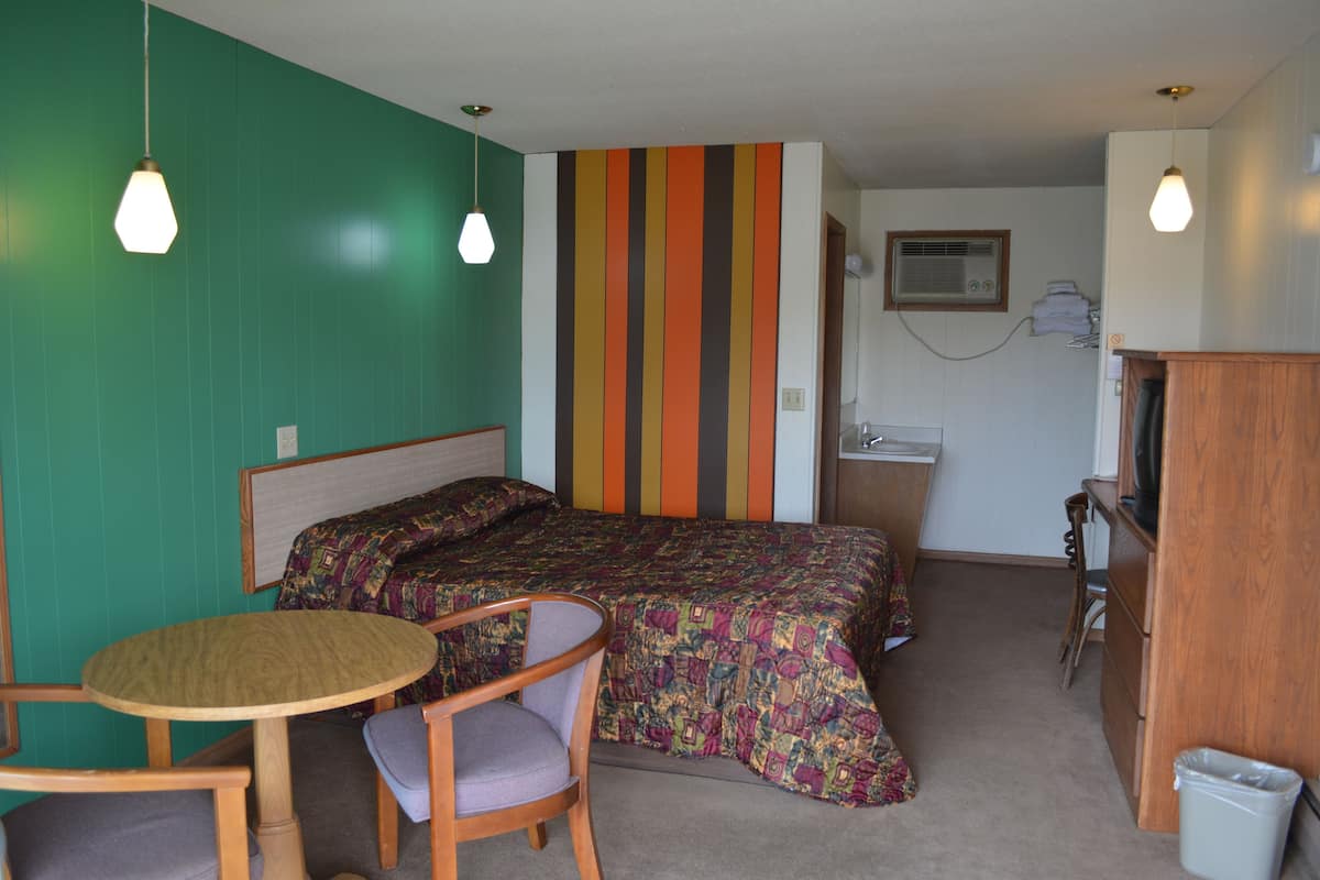 A compact room with a bed, a small table, two chairs, a desk, and a trash bin.
