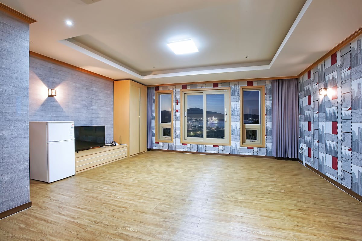 A spacious living area with a large window, a built-in TV, and a refrigerator.