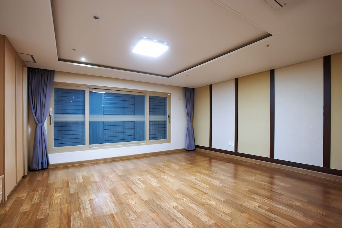 A room with a large window, wooden flooring, and a ceiling light.