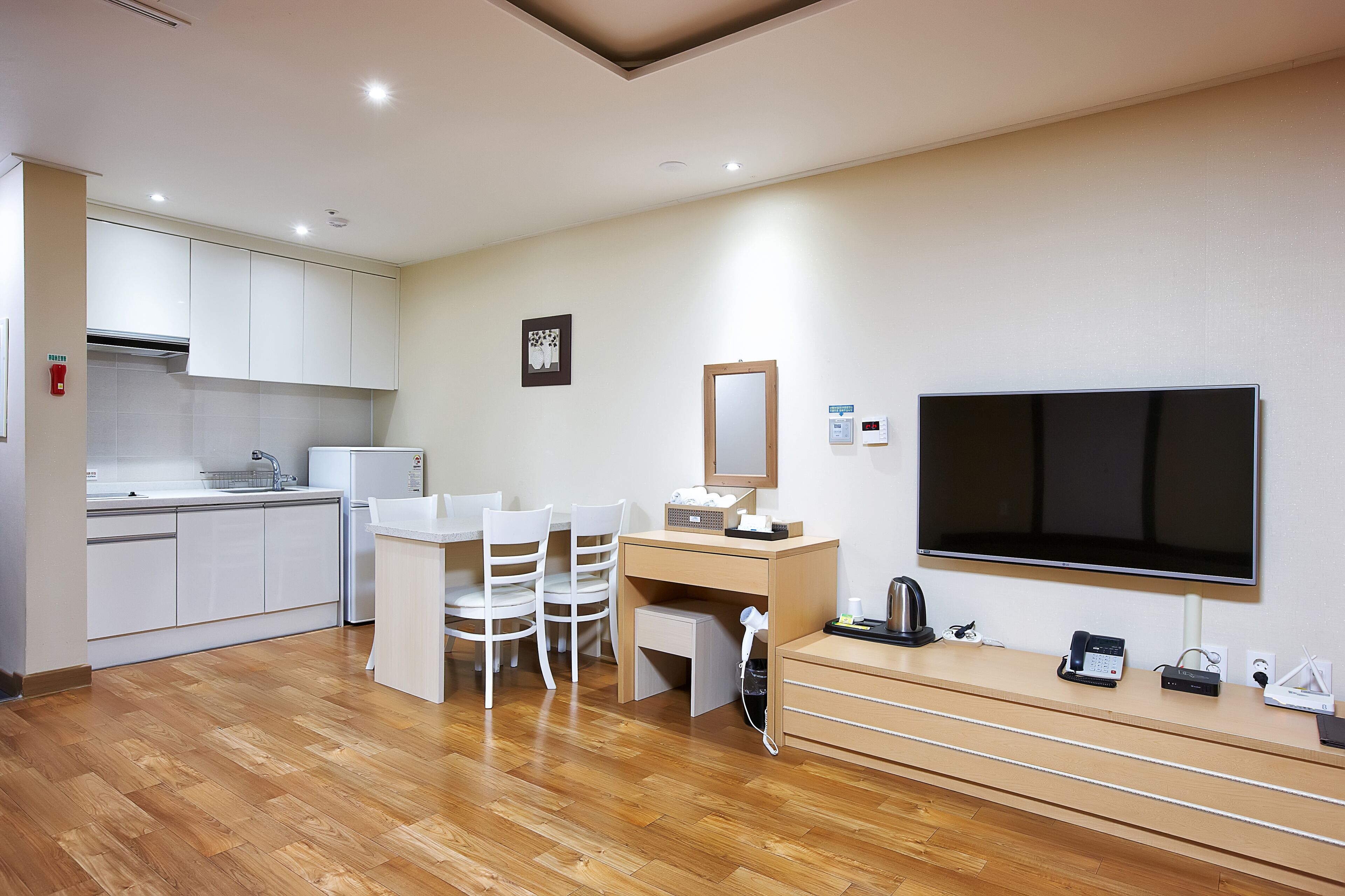 A modern hotel room with a kitchenette, a dining area with chairs, a TV, and a desk with a mirror.