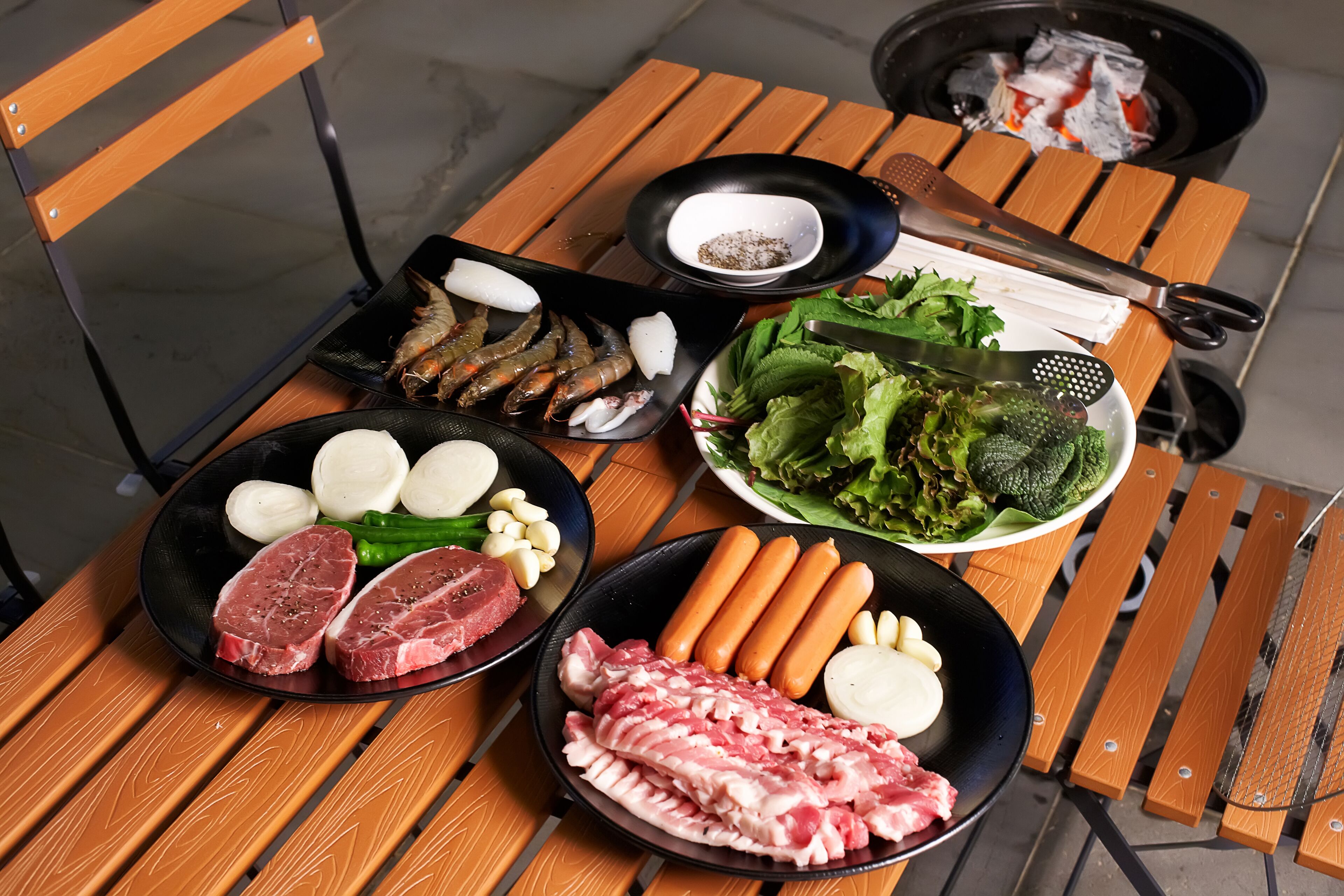 Una mesa con carnes, verduras y una parrilla.