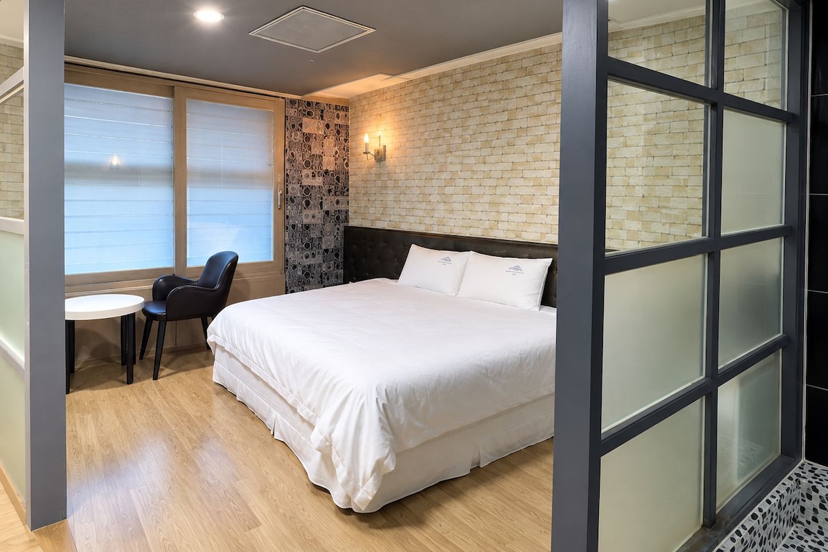 Ein modernes Hotelzimmer mit einem großen Bett, einem kleinen Tisch mit Stuhl und einer Wand mit Ziegelmuster.