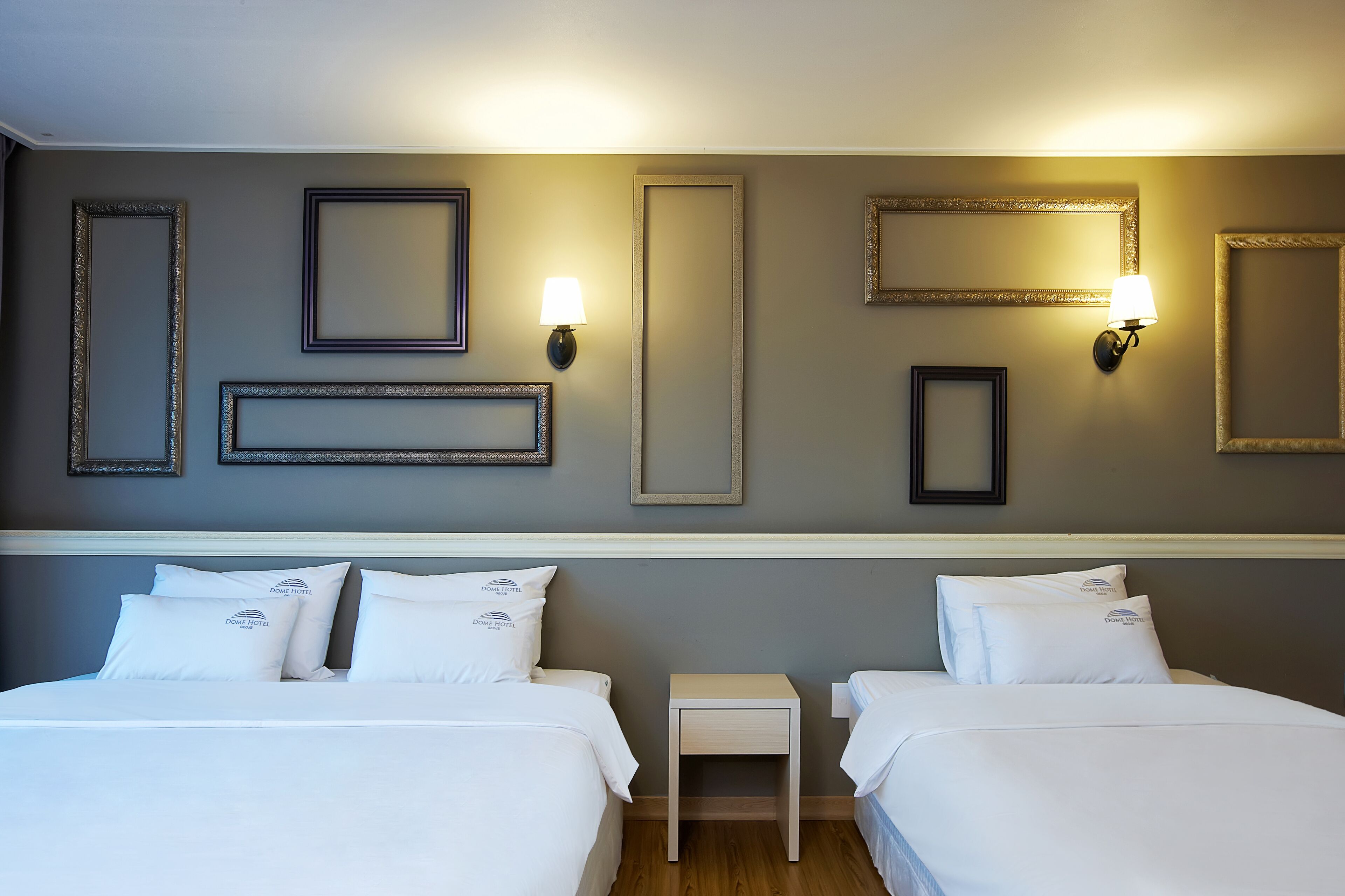 A hotel room with two beds, a nightstand, and wall-mounted lamps.
