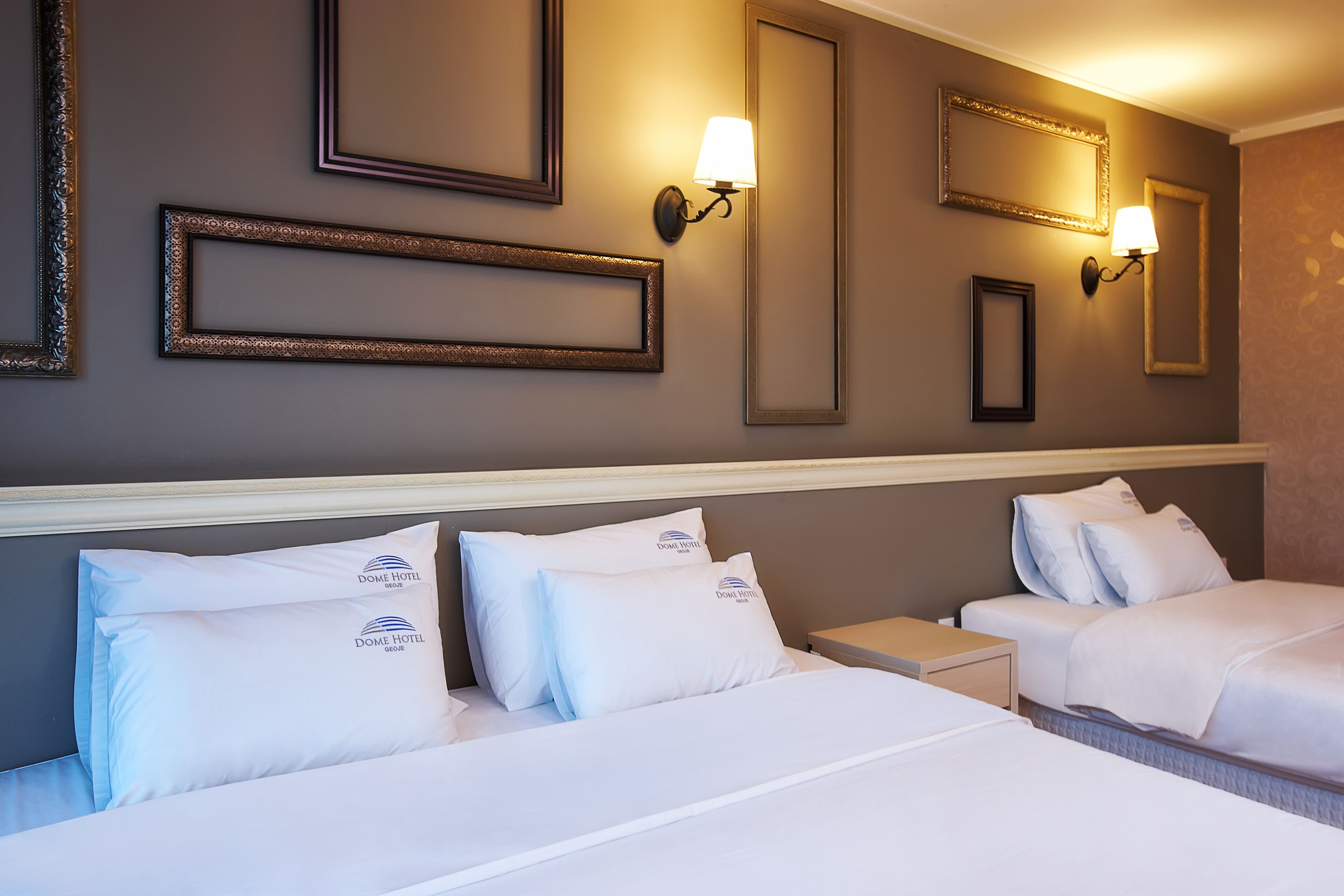 A hotel room with two beds, each with white bedding and pillows, a headboard, and wall-mounted lamps.