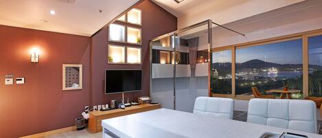 Habitación de hotel moderna con área de cocina, asientos y un gran ventanal con vistas a la ciudad.