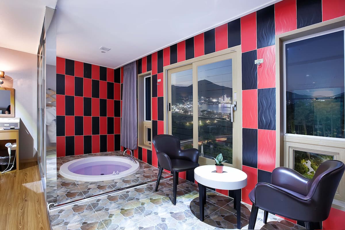 A room with a stone-tiled floor, a black leather chair, a white table, and a glass door leading to a balcony with a city view.