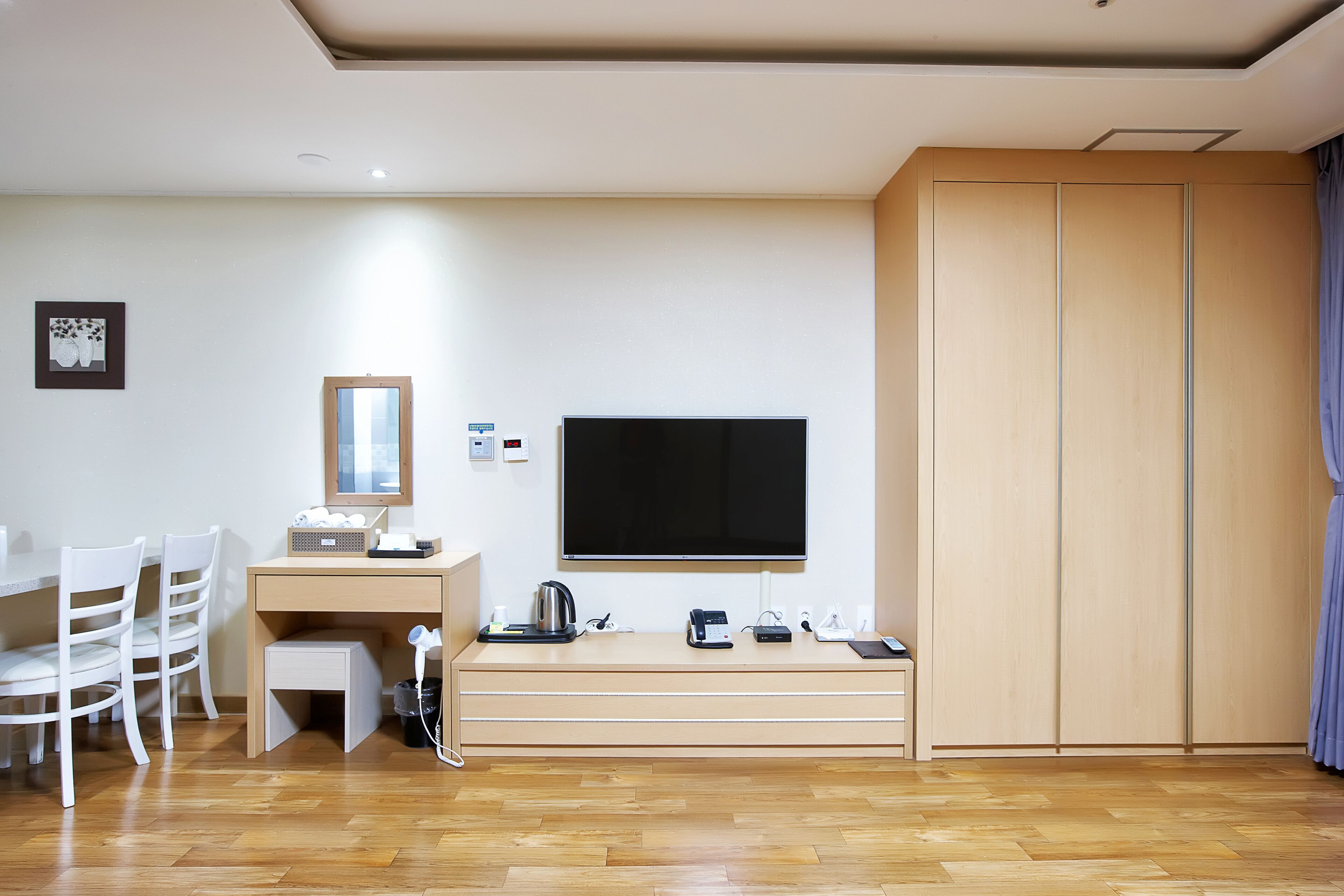 Une chambre moderne dotée d’un bureau en bois, d’un téléviseur à écran plat, d’une armoire et d’un coin repas avec des chaises.