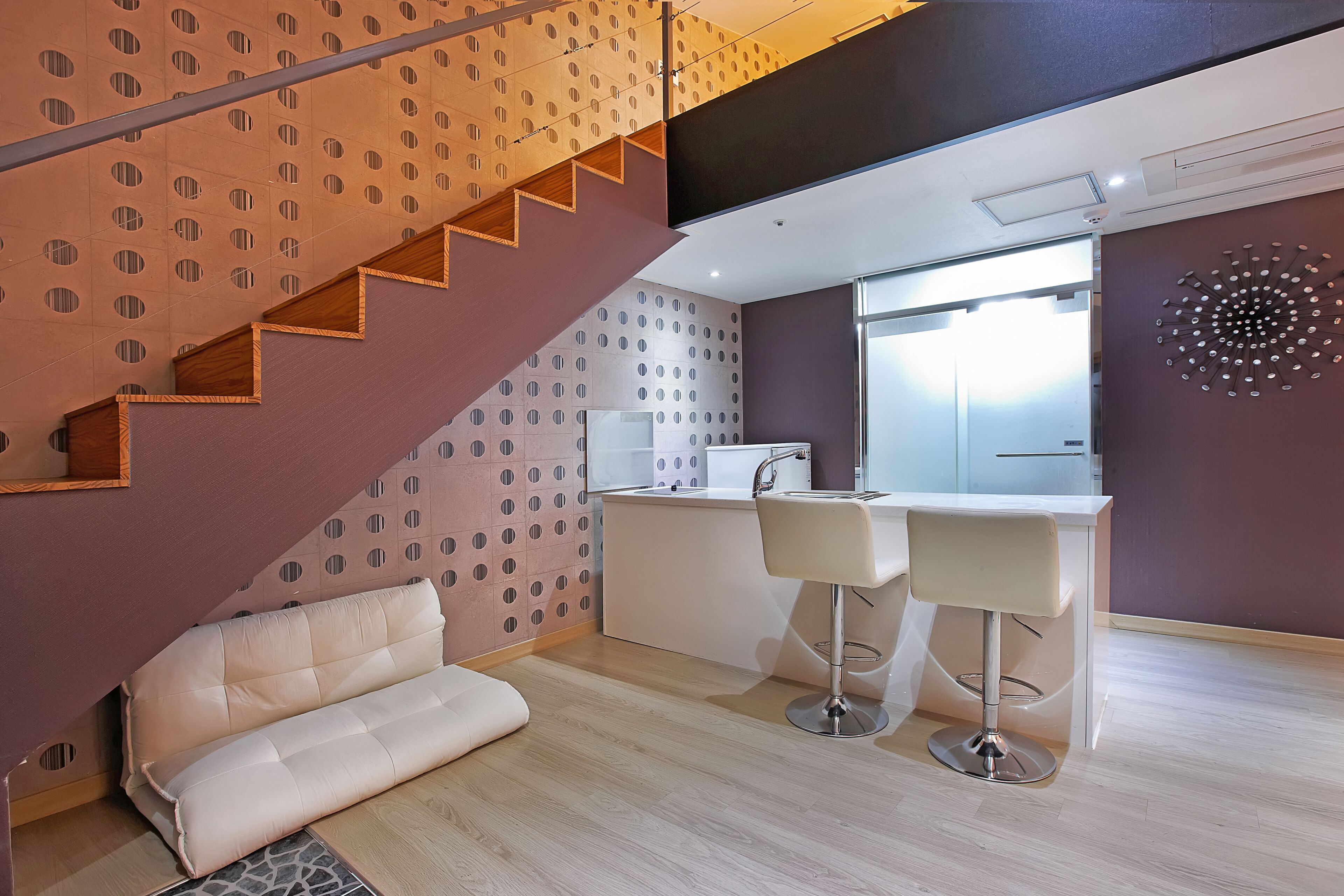 Une cuisine moderne dotée d’un îlot central intégré, de deux tabourets de bar et d’un escalier agrémenté d’un mur au motif original.