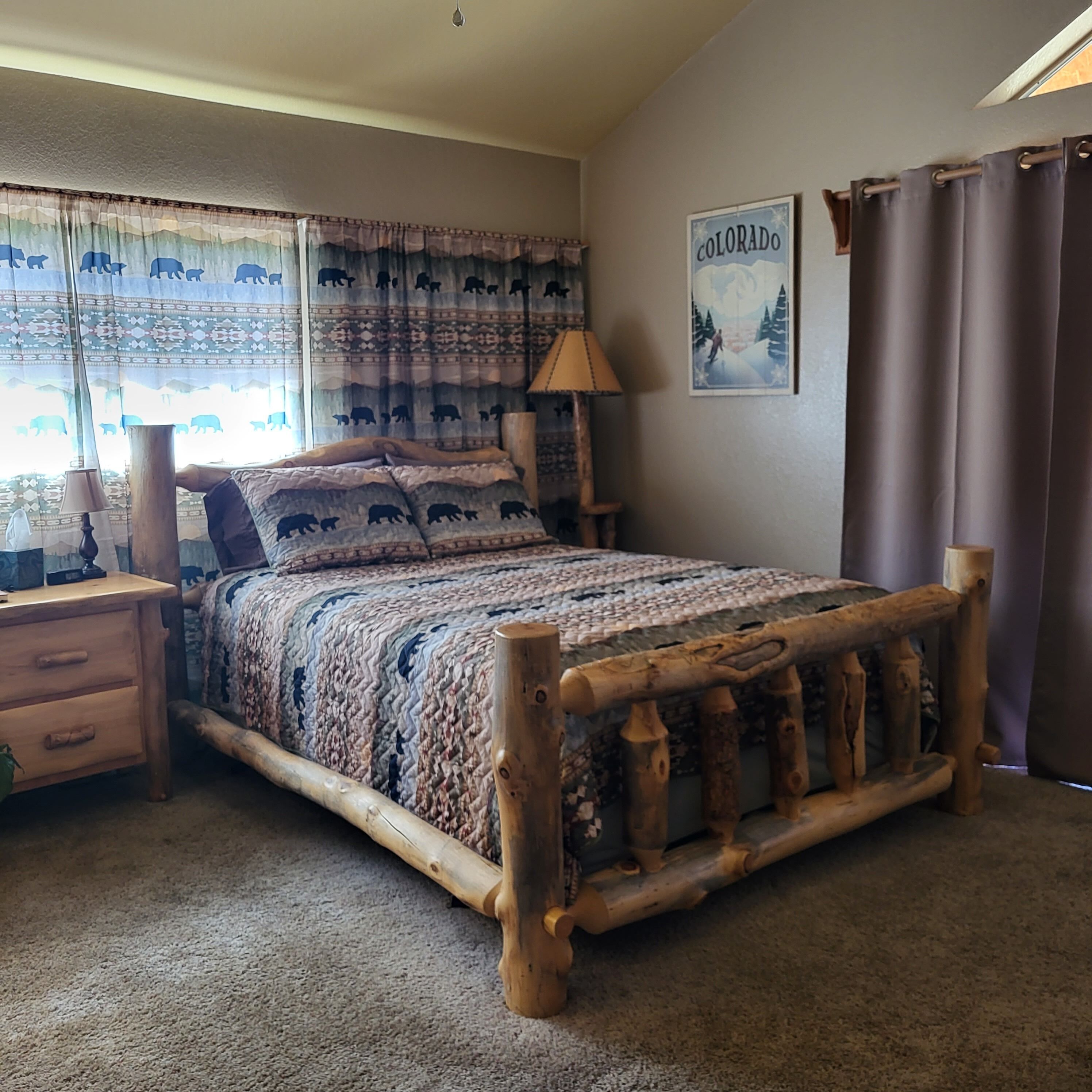 A bedroom with a wooden bed frame, a nightstand, a lamp, and a wall-mounted picture.