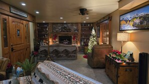 A cozy living room with a fireplace, a Christmas tree, and a large painting on the wall. - Buffalo Peaks B&B (Buena Vista)