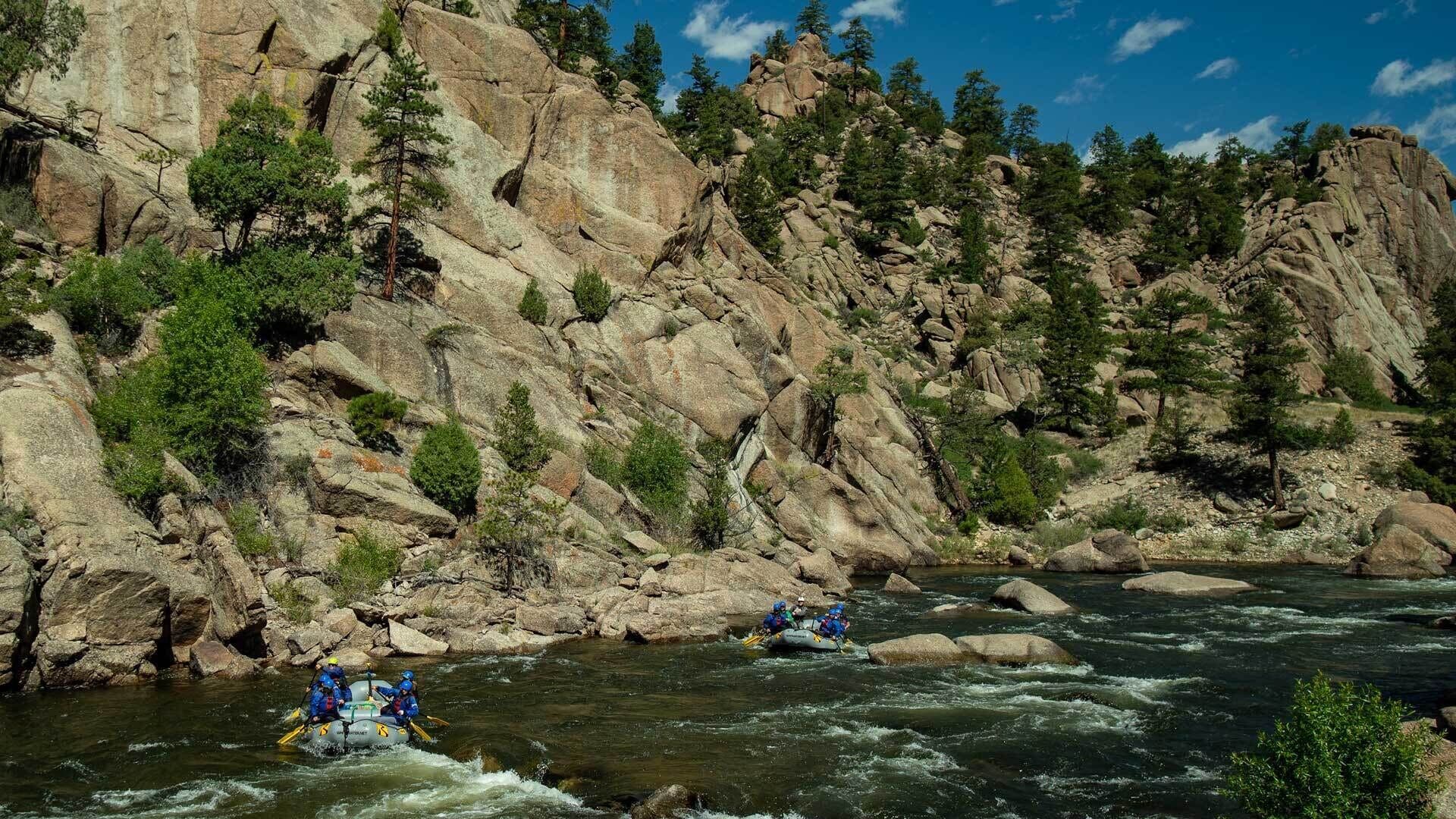 A river with rapids, surrounded by rocky cliffs and sparse vegetation.